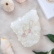 Load image into Gallery viewer, Elegant Kunzite earrings with details in 18k gold-plated 925 sterling silver. Presented on a crystal cluster on a beach.